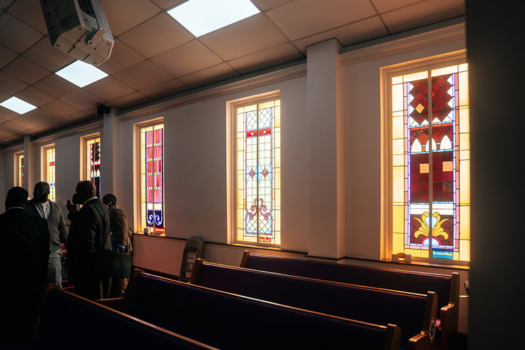 empty church with a few people near the doors. the pews are a royal purple