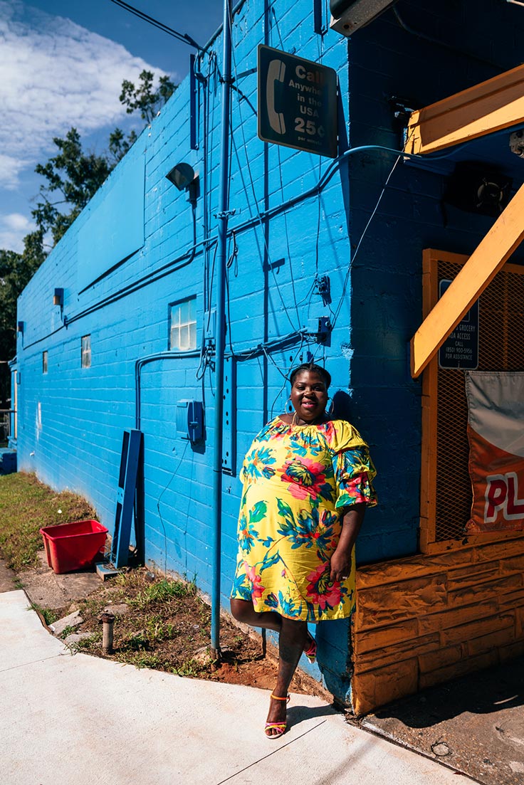 woman in bright yellow outfit standing in front of bright blue corner store