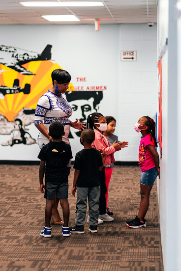 a group of children stand with a woman in a hallway