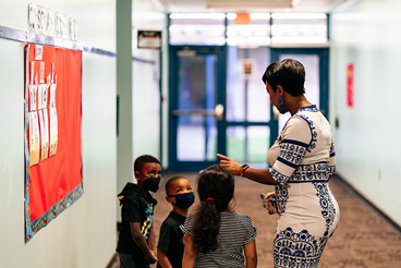 a group of children stand with a woman in a hallway