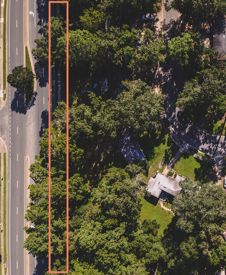 trees and house from above. on the left side of the photo there is a street with a wall outlined in orange.