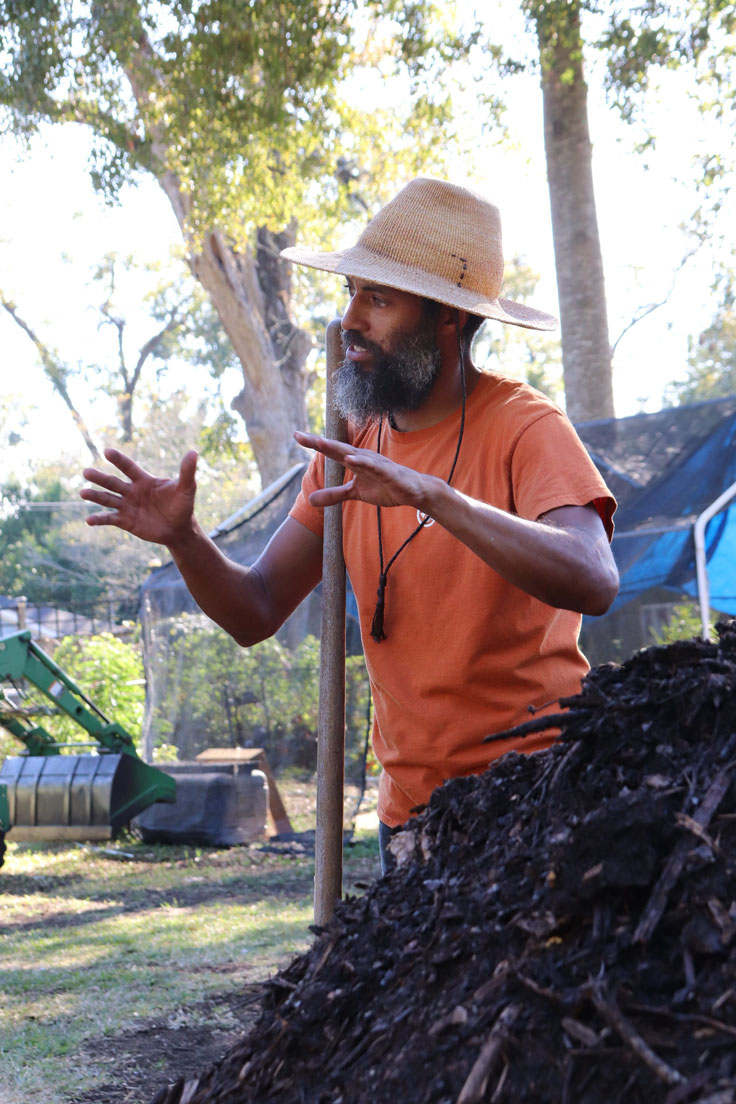 a man in an orange shirt with his hands out speaking to a group