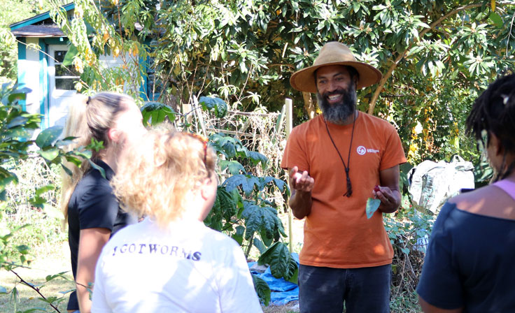 a man in an orange shirt with his hands out speaking to a group