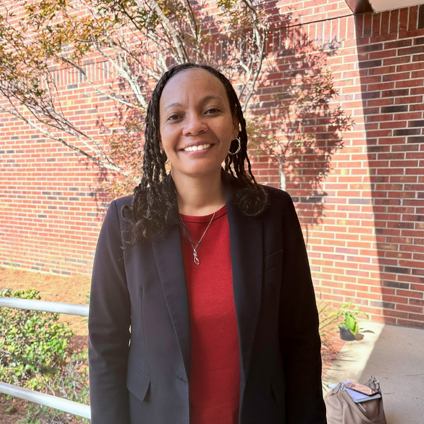 A smiling woman stands outside in front of a red brick wall.