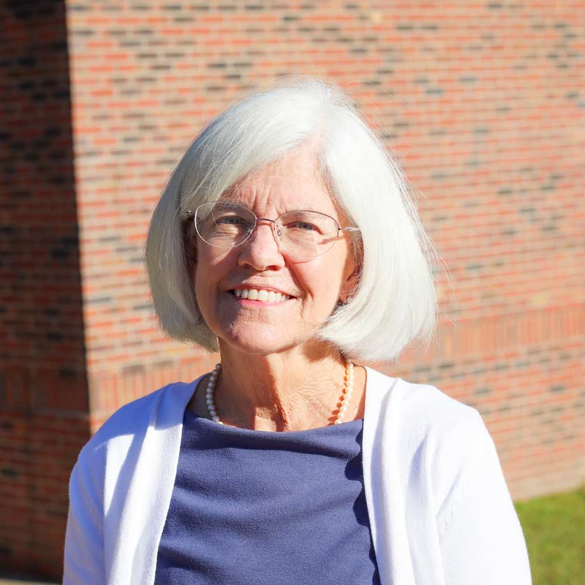 A smiling woman stands outside in front of a red brick wall.