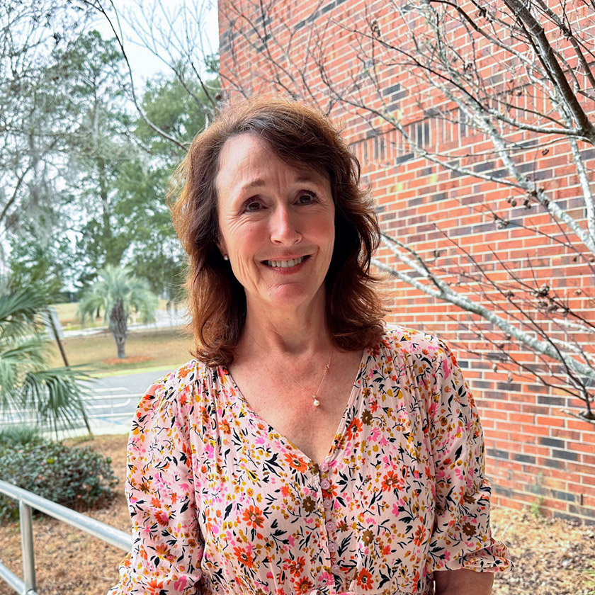 A smiling woman stands in front of a red-brick wall.