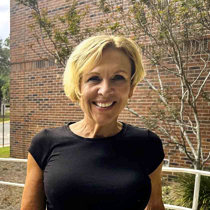 A smiling woman stands outside in front of a red brick wall.