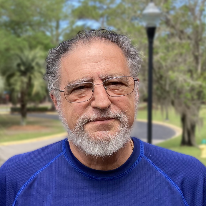 A man stands outside and looks forward while wearing a blue shirt.