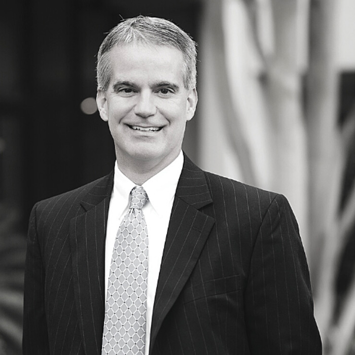 A man smiling in a dark suit and tie.