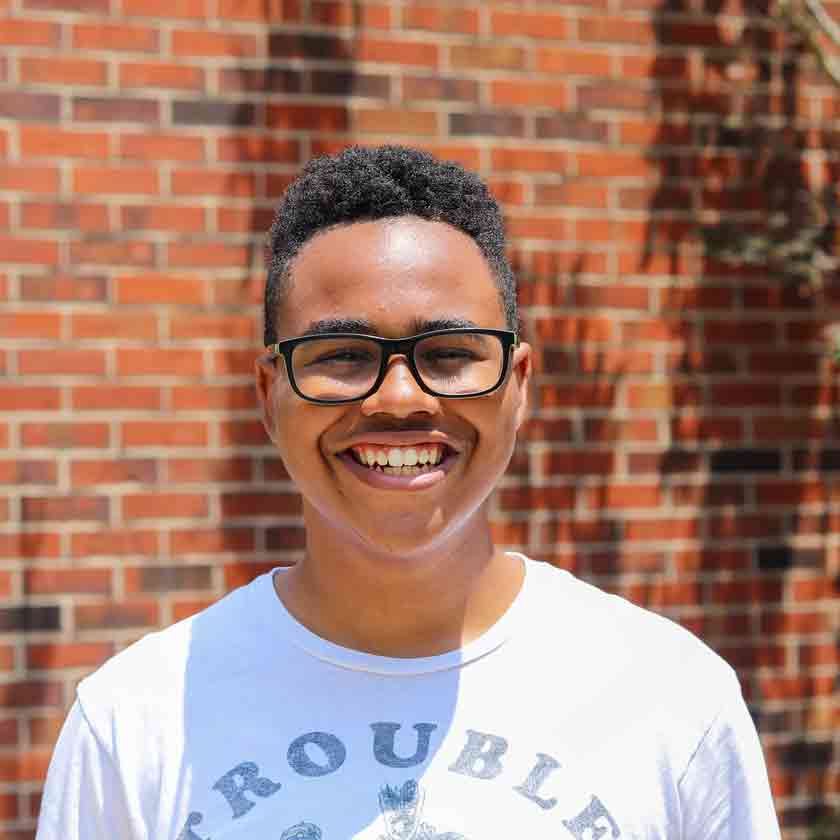 A smiling man stands in front of a red brick wall.