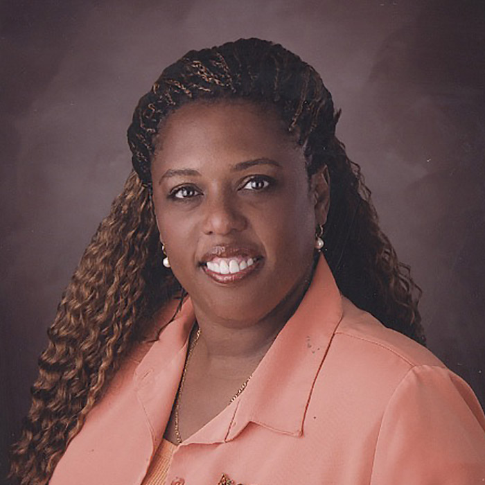 A smiling woman in a peach suit stands in front of a brown backdrop.