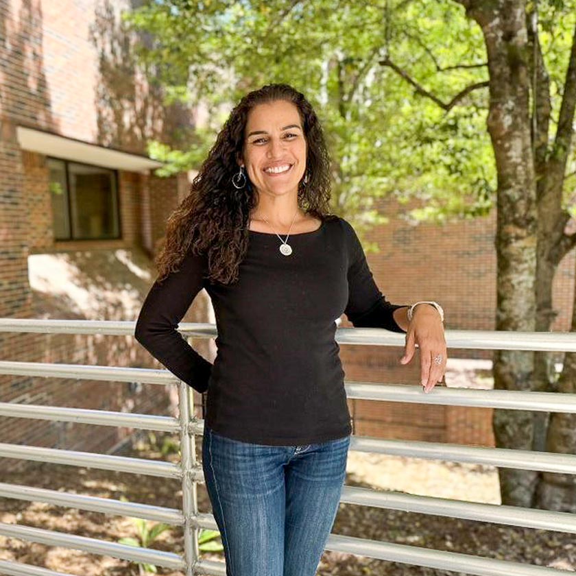 A smiling Woman stands leaned against a railing.