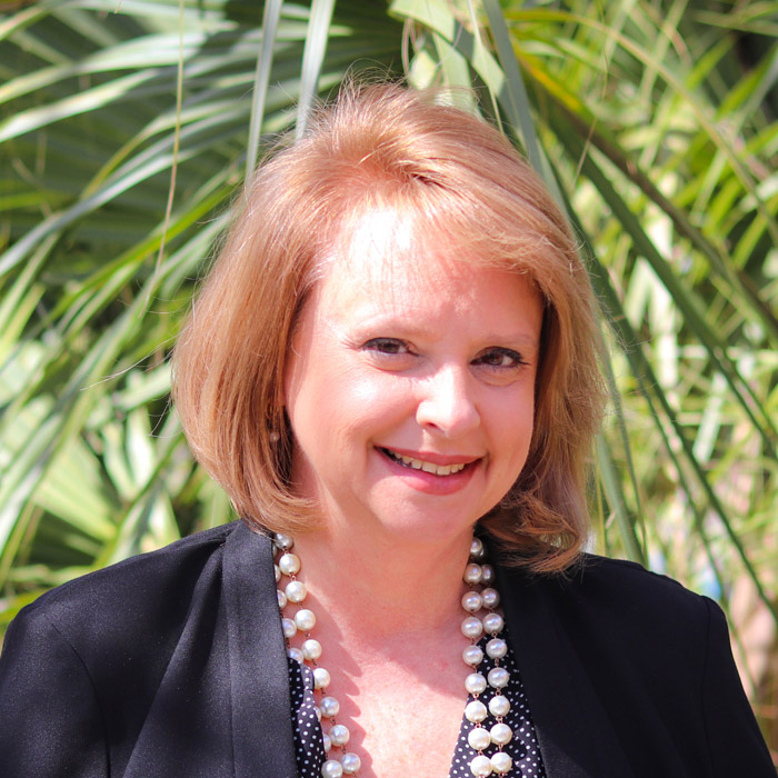 A woman in a blazer is smiling outside.