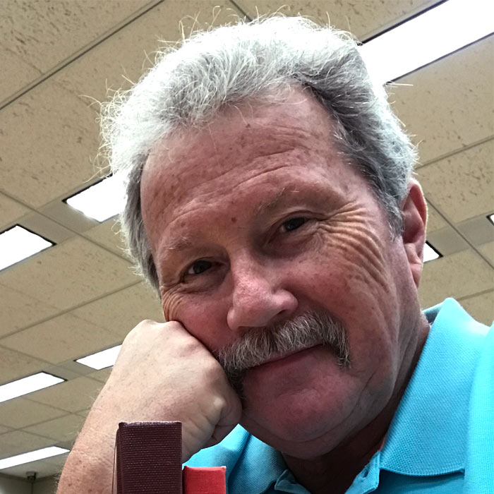 A smiling man looks forward while wearing a teal shirt.