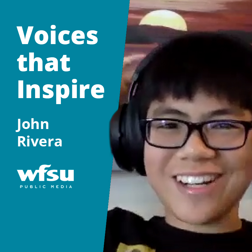 A young man in a black t-shirt wearing large over-the-ear headphones and glasses is smiling.