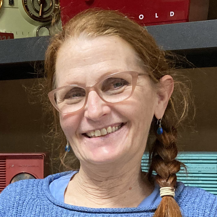 A smiling woman stand in front of a shelf of radios.