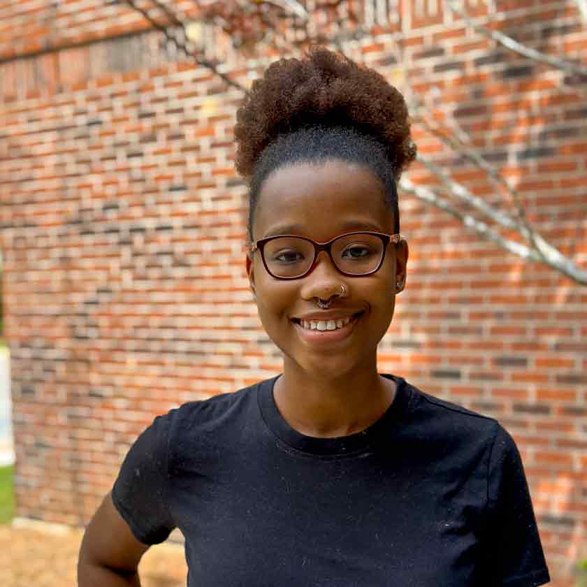 A smiling woman stands in front of a red brick wall.