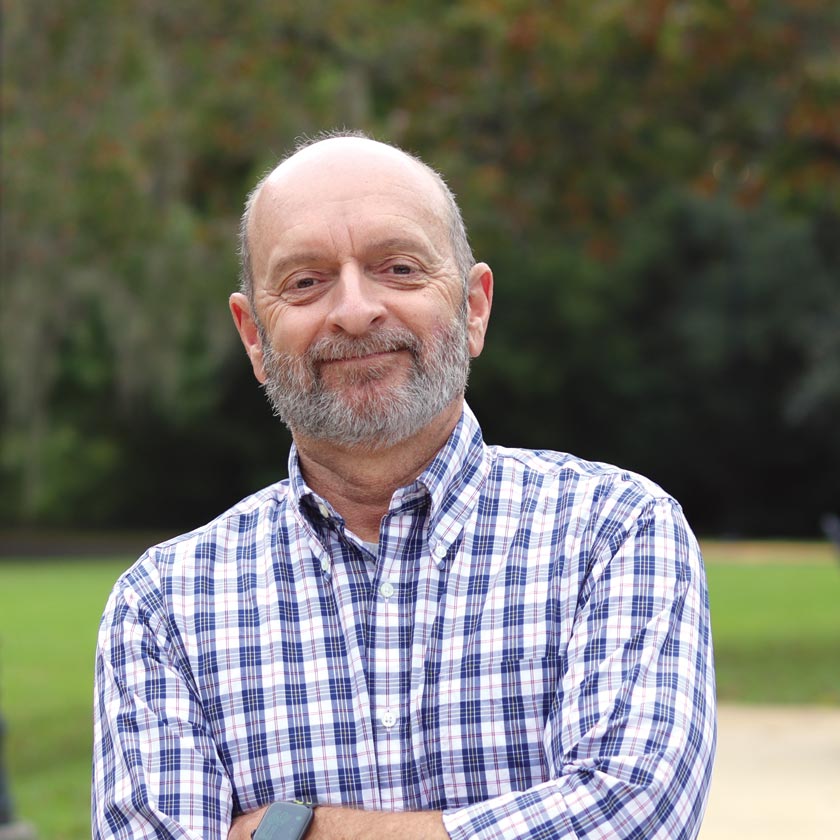 A smiling man in a blue and white checkered shirt smiles.