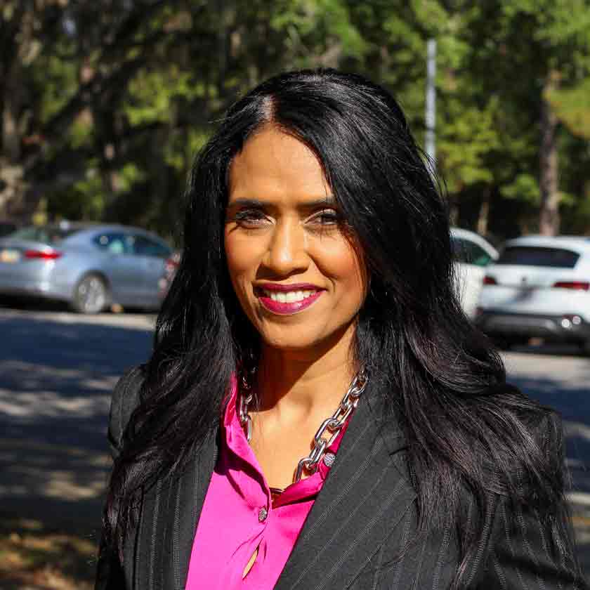 A smiling woman in a dark blazer stares forward.