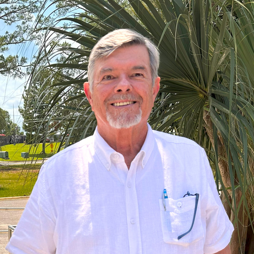 A smiling man in a white shirt stands outside.