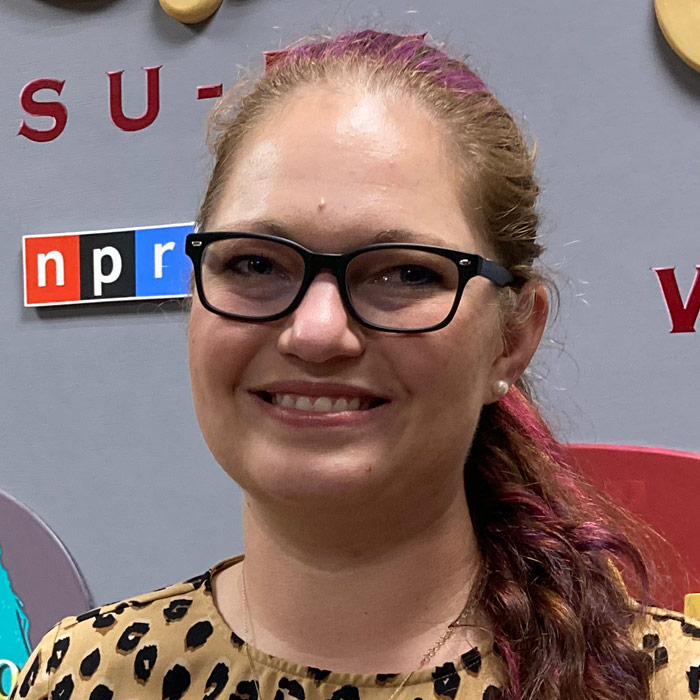 A smiling woman in glasses faces forward.