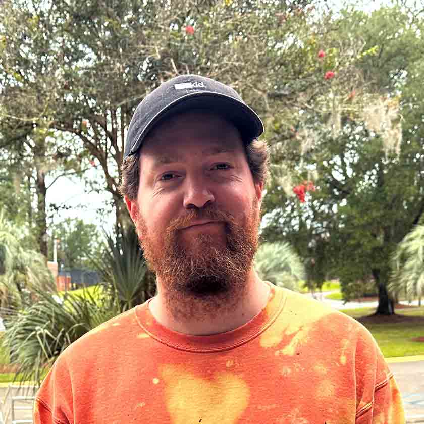 A smiling man in an orange shirt stares forward.