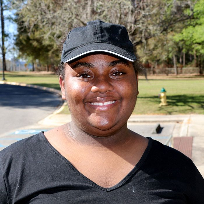 A smiling woman in a baseball cap stands outside.