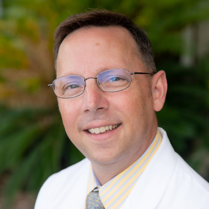 Man smiling in white coat with a shirt and tie.