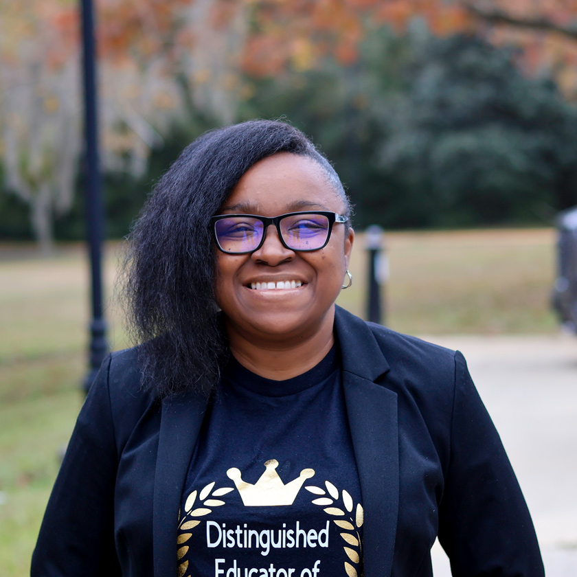 A smiling woman in a black blazer stands outside.