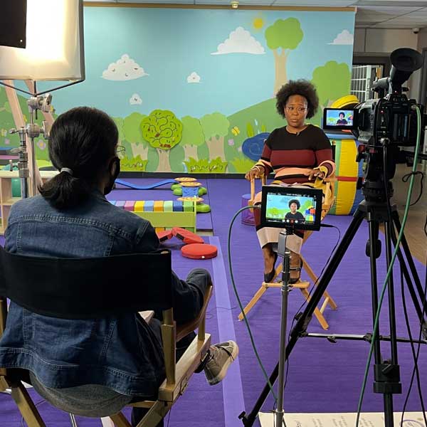 slassroom setting - woman sitting in chair next to video camera in front of another woman speaking in chair 