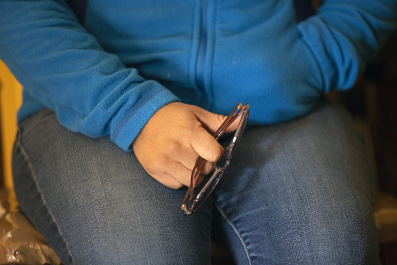 person with hands in lap holding glasses, blue sweatshirt